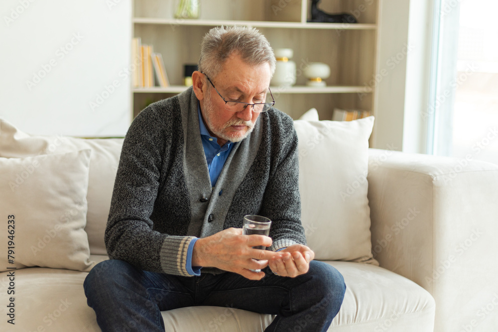 Middle aged senior man holding medical pill and glass of water. Mature old senior grandfather taking medication cure pills vitamin. Age prescription medicine healthcare therapy concept Middle aged senior man holding medical pill and glass of water. Mature old senior grandfather taking medication cure pills vitamin. Age prescription medicine healthcare therapy concept