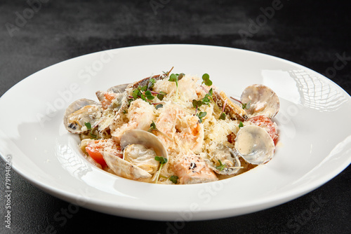 Seafood pasta with vongole, clams, salmon fish and prawns in white plate. Spaghetti marinara with seafood and cheese on dark background. Seafood menu - pasta in mediterrian style on black table.