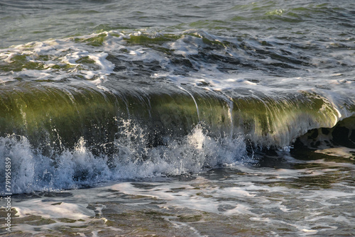 View of the waves of the Black Sea. Clear wavy sea water. Splashes of waves break on the rocks. Sea surf on the beach. The power of water on the sea surf. Splashes of sea waves.