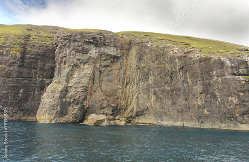 Rocks and caves of the coast near the famous spireTrøllkonufingur  towering rock formation on Vágar Island photo