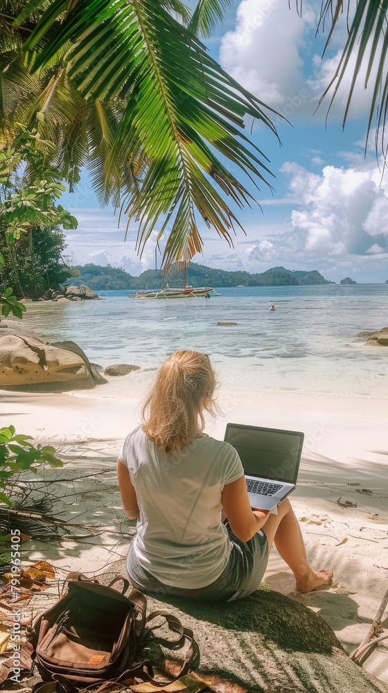 A woman is sitting on the beach and working on her laptop.