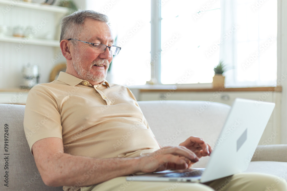 Confident stylish happy middle aged senior man using laptop at home. Stylish older mature 60s beard grandfather sitting at couch looking at computer screen typing chatting reading writing email Confident stylish happy middle aged senior man using laptop at home. Stylish older mature 60s beard grandfather sitting at couch looking at computer screen typing chatting reading writing email