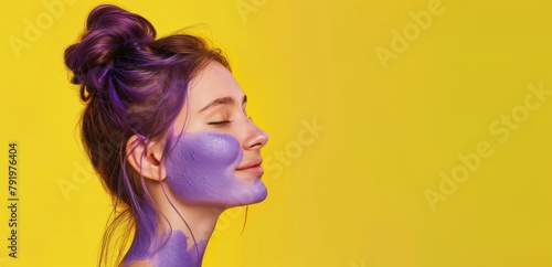 A joyful girl enjoys a purple face mask against a yellow background.