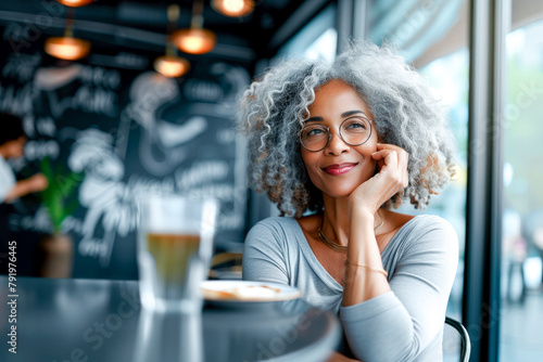A woman with curly hair and glasses is sitting at a table with a cup of tea