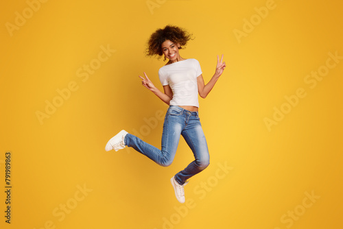 African-american joyful lady jumping and gesturing peace