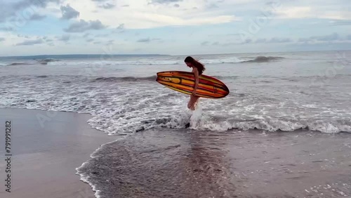 Female surfer. Young woman surfer in bikini goes along tropical beach confidently carrying surfing board on the at sunset. Girl in swimsuit enjoying water sport. High quality FullHD footage