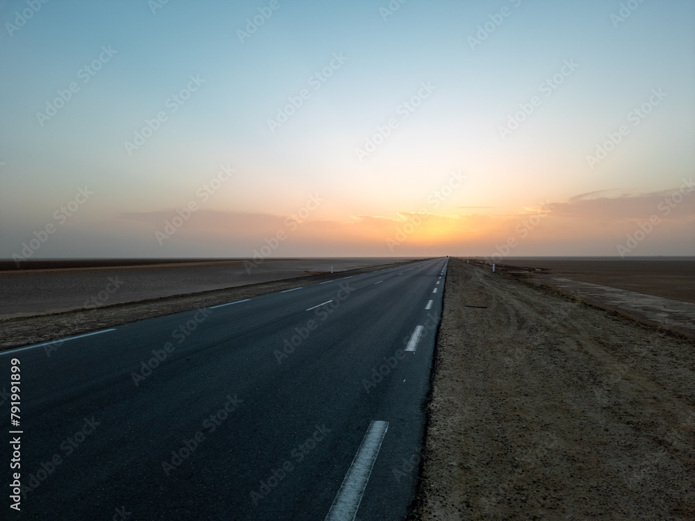 Beautiful colourful sunset over endless empty road in middle of desert. Asphalt highway in Tunisia, North Africa.	