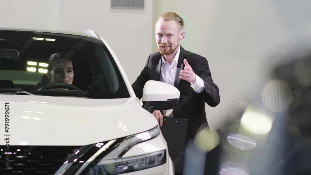 A professional salesman in a business suit communicates with a happy client in a modern car dealership. Automotive business, trade, dealership. A professional salesman in a business suit communicates with a happy client in a modern car dealership. Automotive business, trade, dealership.