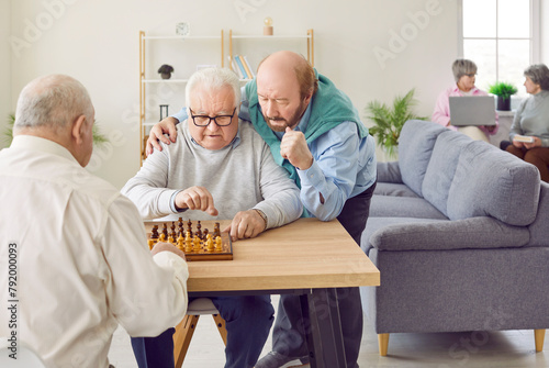 Group of happy men senior people playing chess in nursing home sitting at the table. Pensioners spending leisure time together playing board games. Leisure in retirement home concept.