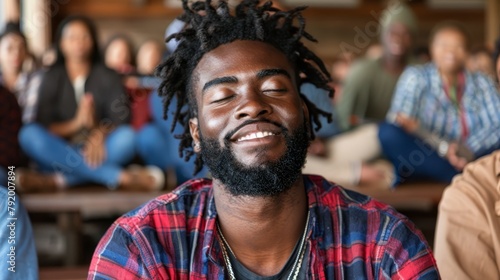   A man with dreadlocks sits before a crowd with closed eyes photo