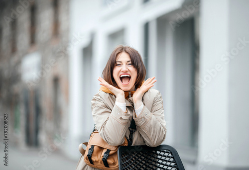 Exuberant Young Woman with Hands on Cheeks, Excitedly Smiling on Urban Chair photo