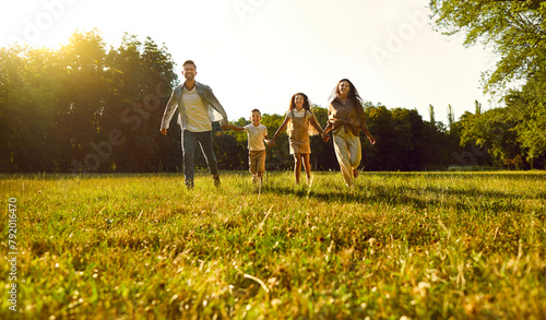 Happy smiling family with two kids boy and girl walking in summer park enjoying beautiful nature. Mother, father and their children runnung outdoors spending time together at sunset. photo