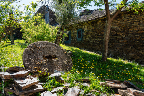 Old millstone in a meadow next to stone houses, black villages, Majaelrayo. photo