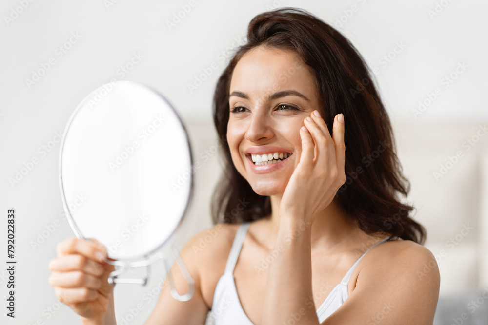 Lady inspecting face in mirror, touching cheek Lady inspecting face in mirror, touching cheek