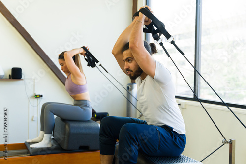 Two people engaging in a pilates workout using a reformer bed in a bright studio setting