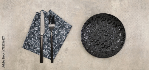 Empty black gray plate, fork; knife, napkin on marble rustic concrete background. Top view, flat lay.