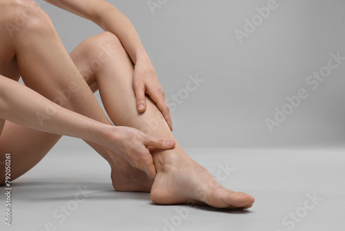 Woman suffering from leg pain on grey background, closeup. Space for text © New Africa