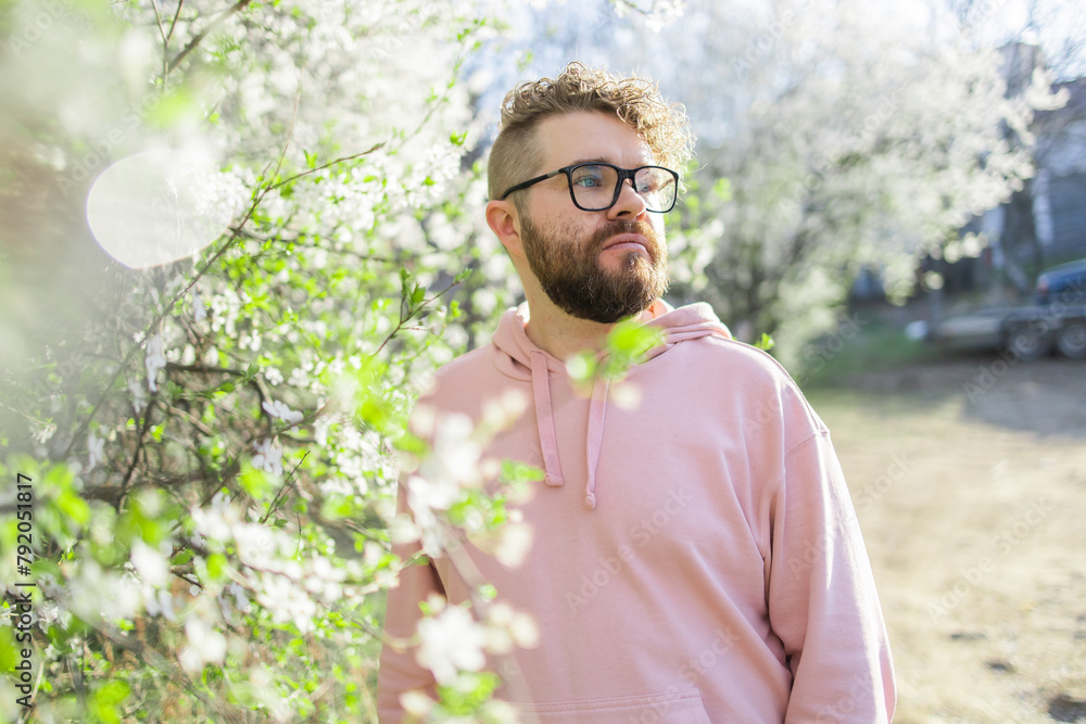 Male bearded man standing under branches with flowers of blooming almond or cherry tree in spring garden. Spring blossom. Copy space Male bearded man standing under branches with flowers of blooming almond or cherry tree in spring garden. Spring blossom. Copy space