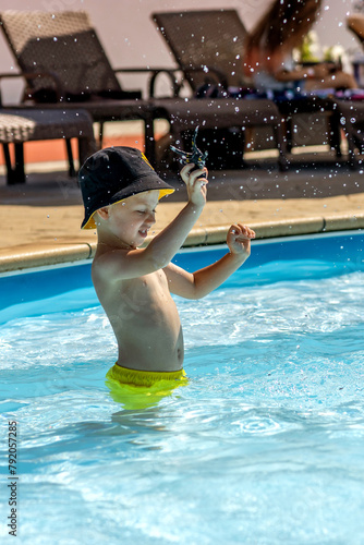 A child plays in the pool, has fun with splashes, hitting the water.