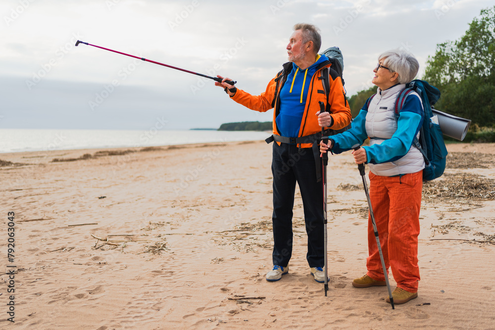 Naklejka premium Hiking tourism adventure. Senior couple man woman enjoying outdoor recreation hiking on beach. Happy old people backpackers hikers enjoy walking hike trekking tourism active vacation beauty of nature