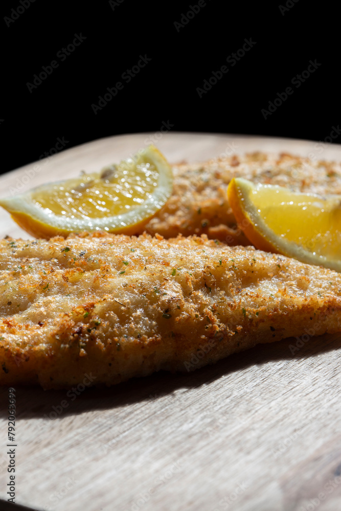 Tempura battered cod fillets coated with herbs and lemon with a slice of lemon. On a wooden chopping board.
