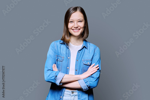 Young confident woman with crossed arms on gray background