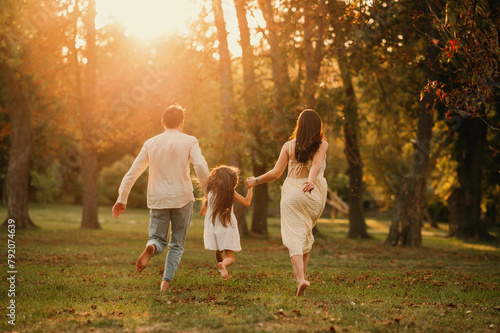 Young family of three are holding hands and running barefoot in a park together. Backview shot.