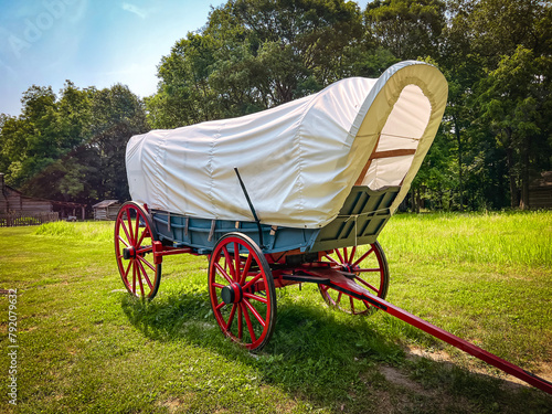 Rear view of a 19th century style horse-drawn carriage or covered wagon set against a green rural nature background.