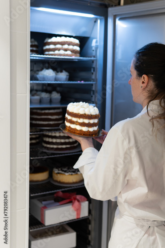 Bakery worker inserts Red Velvet cake into a fridge full of cupcakes, cakes and desserts. one with a gift bow for Valentine's Day