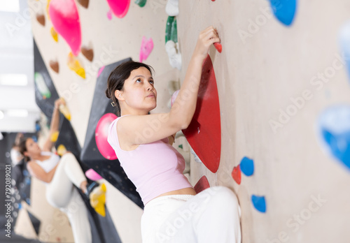 Young central asian woman in sportswear practices rock climbing at climbing wall