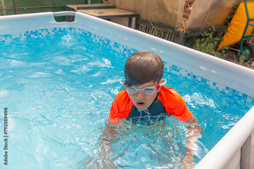 Boy in pool catching breath after swimming, water droplets around as he surfaces in a sunny backyard pool