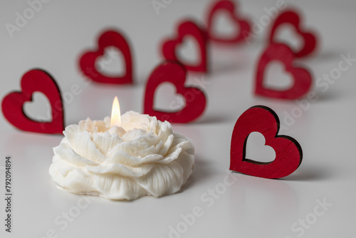 Handmade soy wax candle in flower shape and red hearts on white background. Valentine's day, romance, love concept.