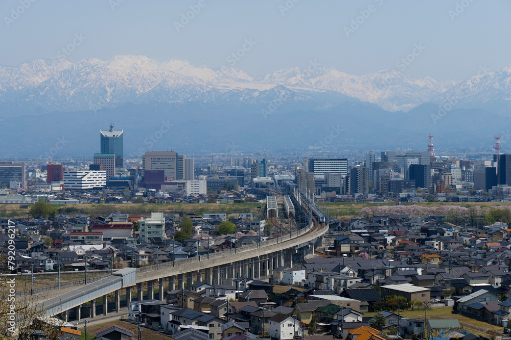 Obraz premium 満開の桜春霞の北アルプス立山連峰と北陸新幹線の見える富山市街地