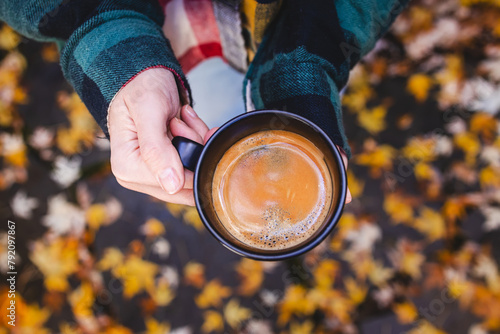 Female hand holding a cup of fresh brewed coffee with yellow leaves on the background