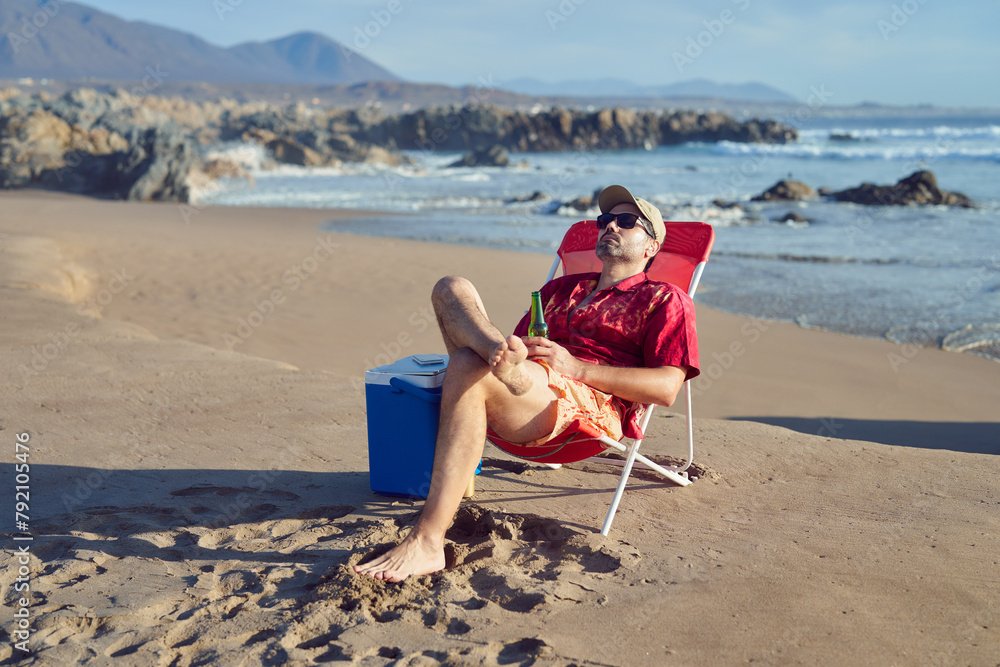 mature man sitting alone, relaxed holding a beer, eyes closed, enjoying the beach and nature
