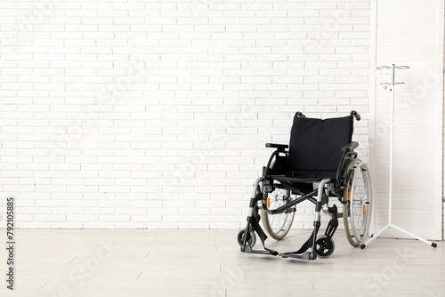 Empty wheelchair with stand for IV drip near white brick wall