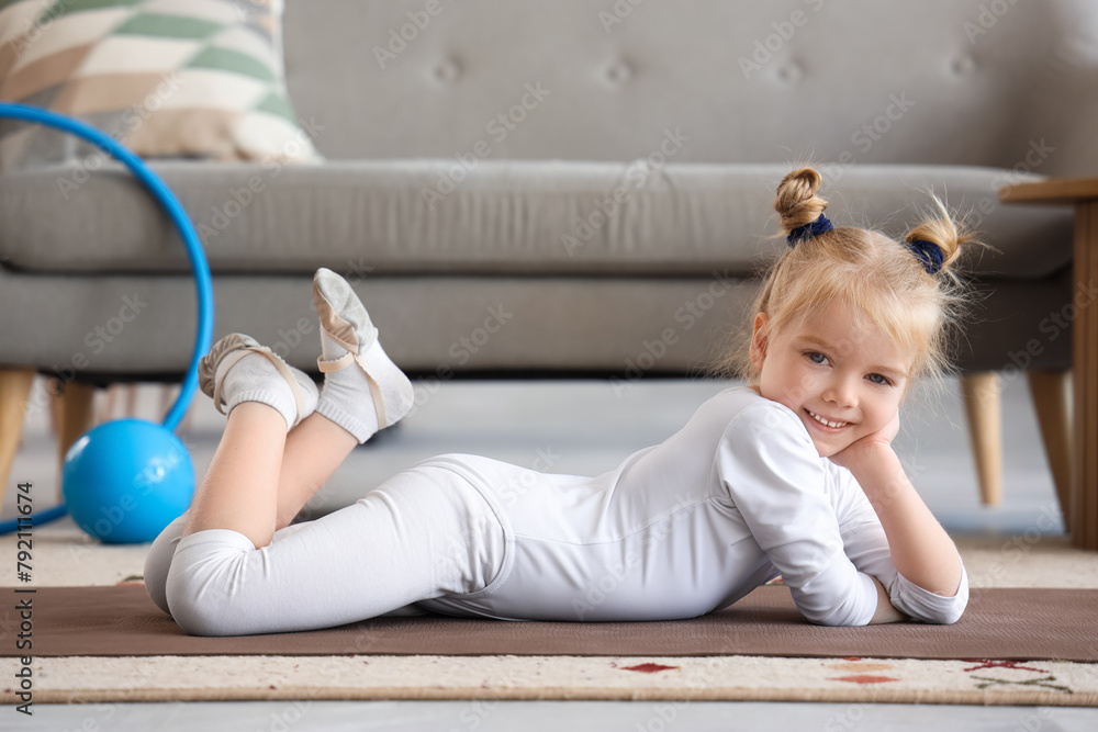 Naklejka premium Cute little girl lying on fitness mat at home