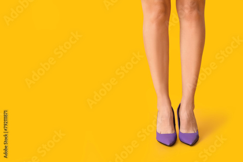 Legs of young woman in stylish purple high heels on yellow background