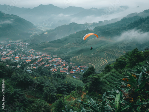 A paraglider flies over rolling hills and a quaint village shrouded in mist.