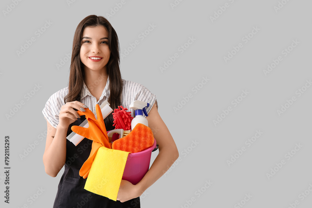 Young woman with cleaning supplies on grey background Young woman with cleaning supplies on grey background