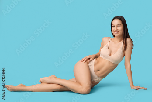 Beautiful young woman in beige underwear sitting on blue background