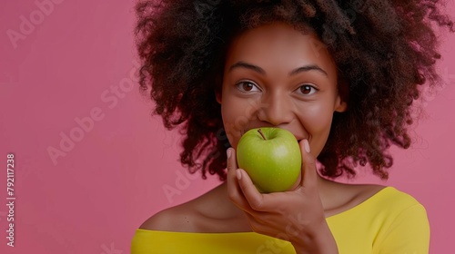 happy woman in bright yellow top biting green apple healthy eating and weight loss concept on pink background
