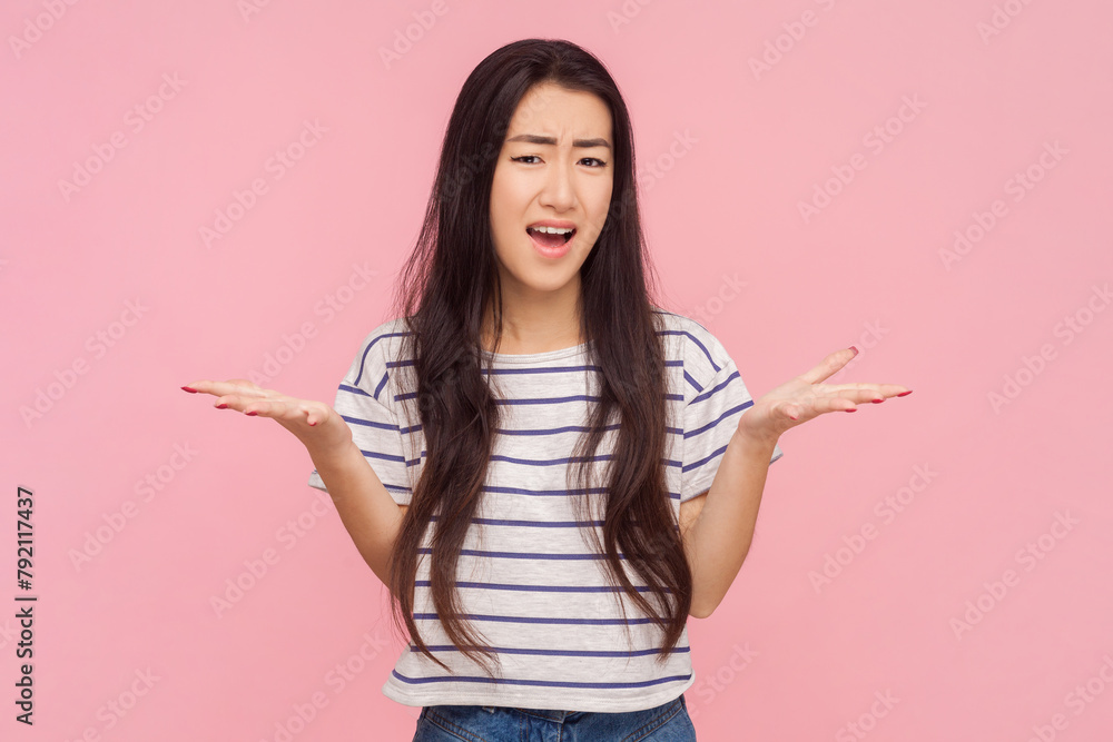 Portrait of shocked unhappy woman with long brunette hair asking what grimacing arguing with somebody, wearing striped T-shirt. Indoor studio shot isolated on pink background. Portrait of shocked unhappy woman with long brunette hair asking what grimacing arguing with somebody, wearing striped T-shirt. Indoor studio shot isolated on pink background.