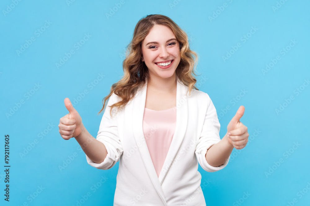 Portrait of satisfied delighted smiling blond woman with wavy hair showing like gesture positive feedback of service, wearing white shirt. Indoor studio shot isolated on blue background. Portrait of satisfied delighted smiling blond woman with wavy hair showing like gesture positive feedback of service, wearing white shirt. Indoor studio shot isolated on blue background.