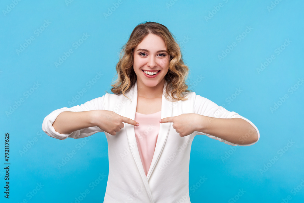 Portrait of happy joyful woman with wavy hair looking at camera with satisfied expression pointing at herself with delighted face wearing white shirt. Indoor studio shot isolated on blue background. Portrait of happy joyful woman with wavy hair looking at camera with satisfied expression pointing at herself with delighted face wearing white shirt. Indoor studio shot isolated on blue background.