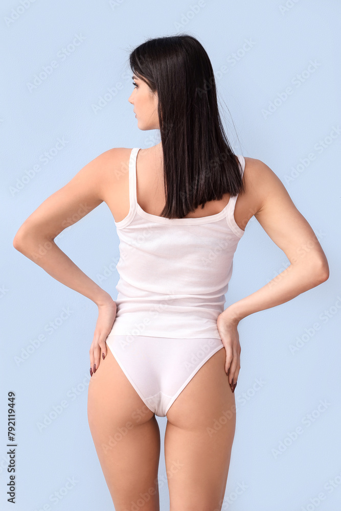 Fototapeta premium Beautiful young woman in white underwear on blue background, back view