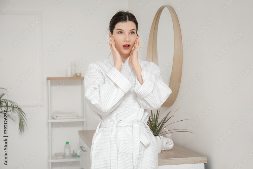 Beautiful young woman in bathrobe doing face building exercise at home Beautiful young woman in bathrobe doing face building exercise at home