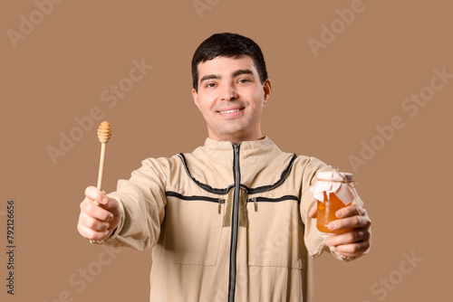 Male beekeeper with honey and spoon on brown background photo