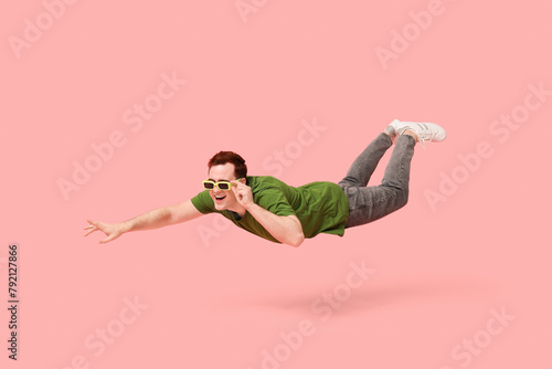 Joyful young man in sunglasses flying on pink background © Pixel-Shot