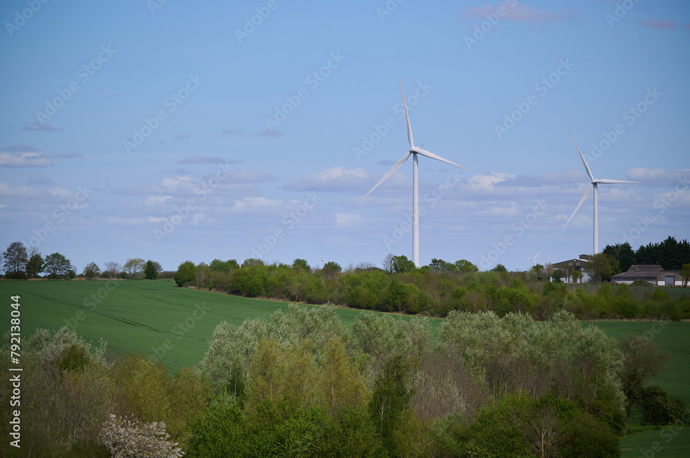 Fototapeta premium Two wind turbines over English countryside against blue sky with small clouds